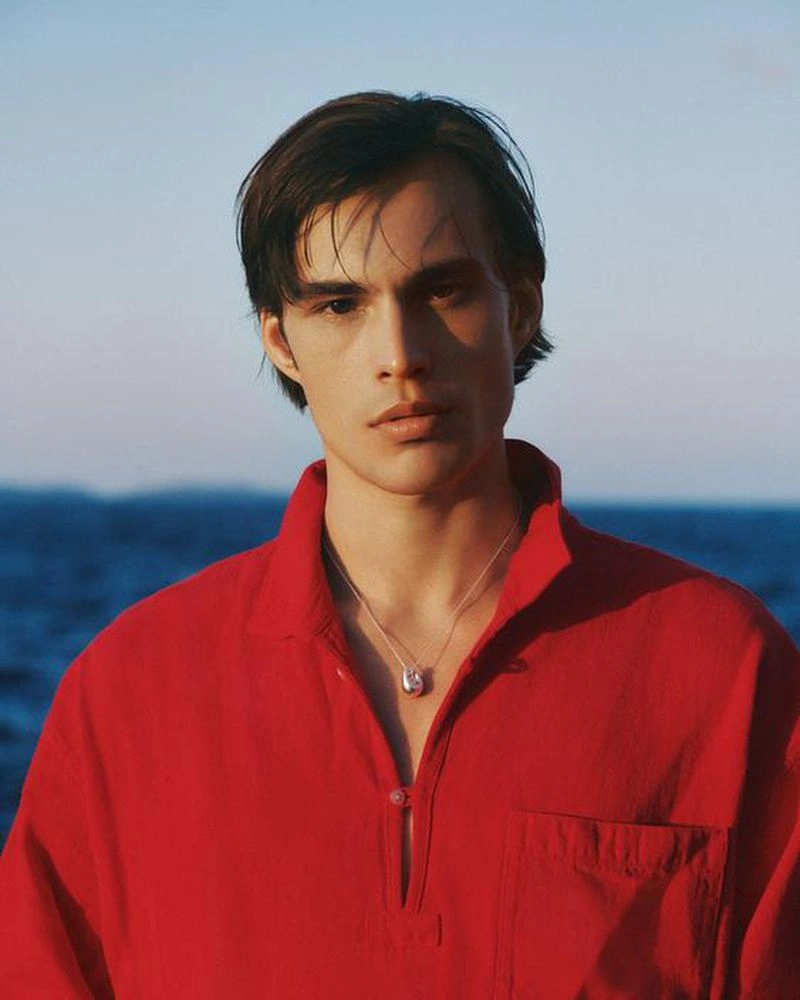 Portrait of a man wearing a bright red collared shirt with a silver necklace against an out of focus blue ocean background.