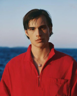 Portrait of a man wearing a bright red collared shirt with a silver necklace against an out of focus blue ocean background.