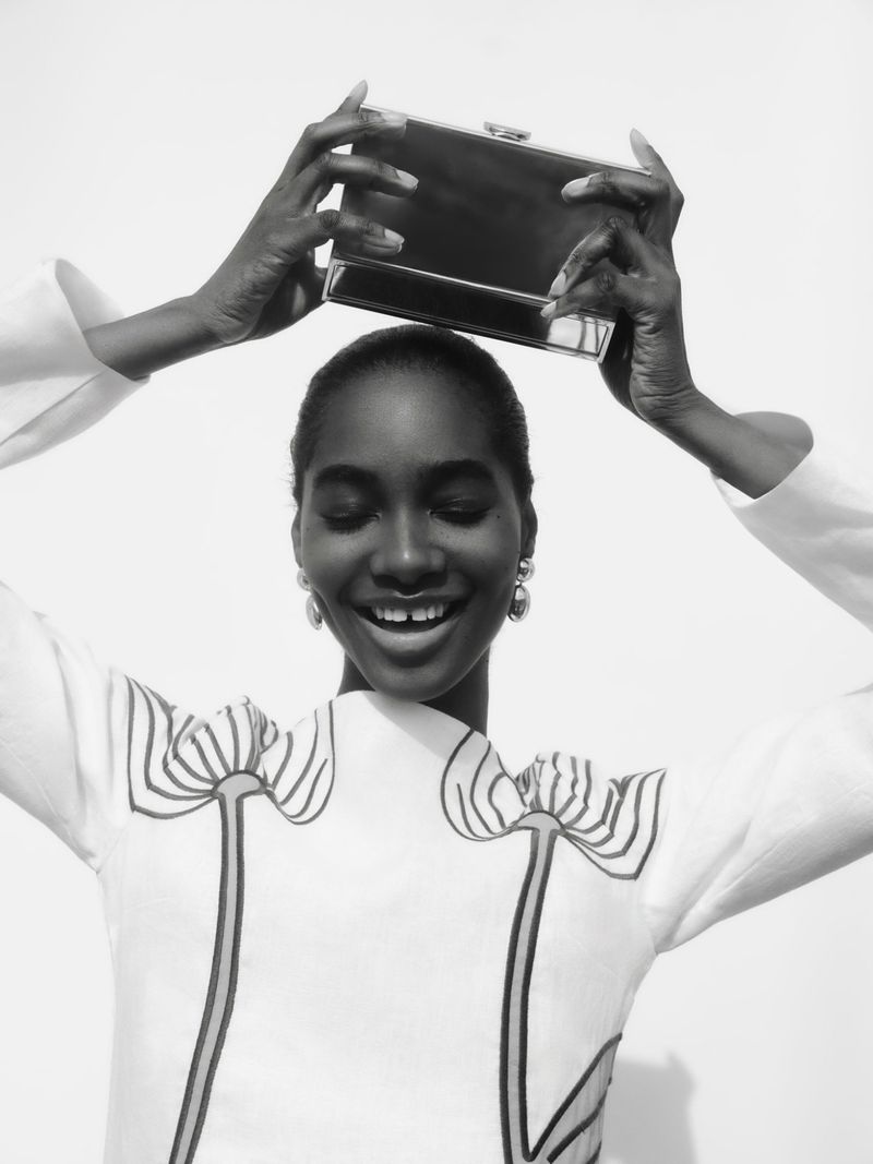 Smiling model holding a dark rectangular clutch above her head against a plain white background for Tuckernuck