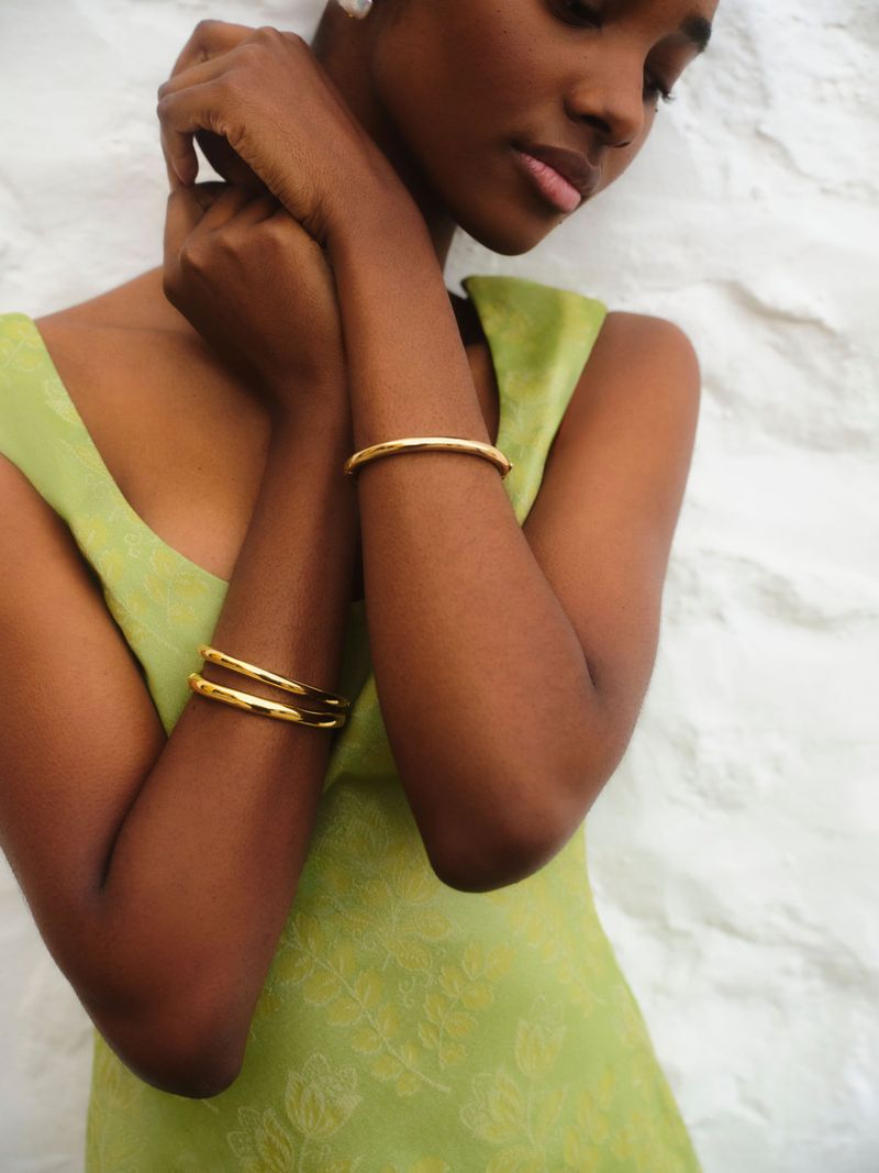Model in green dress wearing gold bracelets posing against a textured white background for Tuckernuck