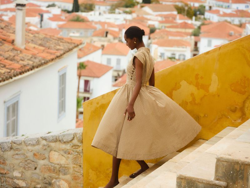 Model in a patterned midi dress descending stone stairs against a Mediterranean town backdrop