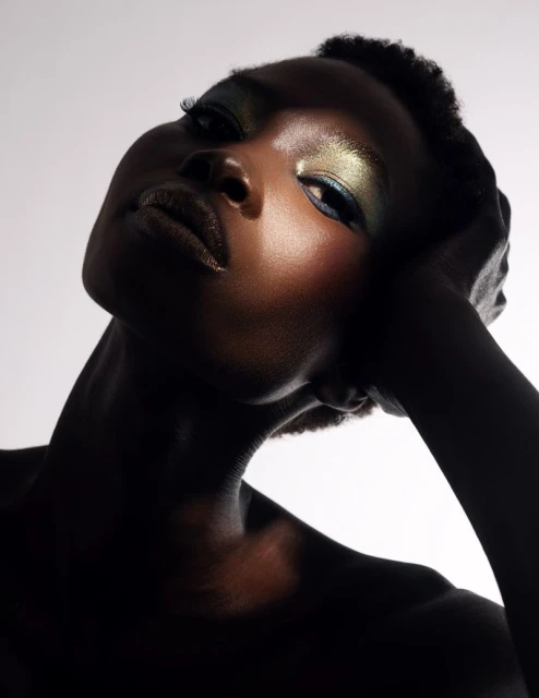 Close-up portrait of a Black woman with shimmering metallic eyeshadow and glossy dark lips against a white background.