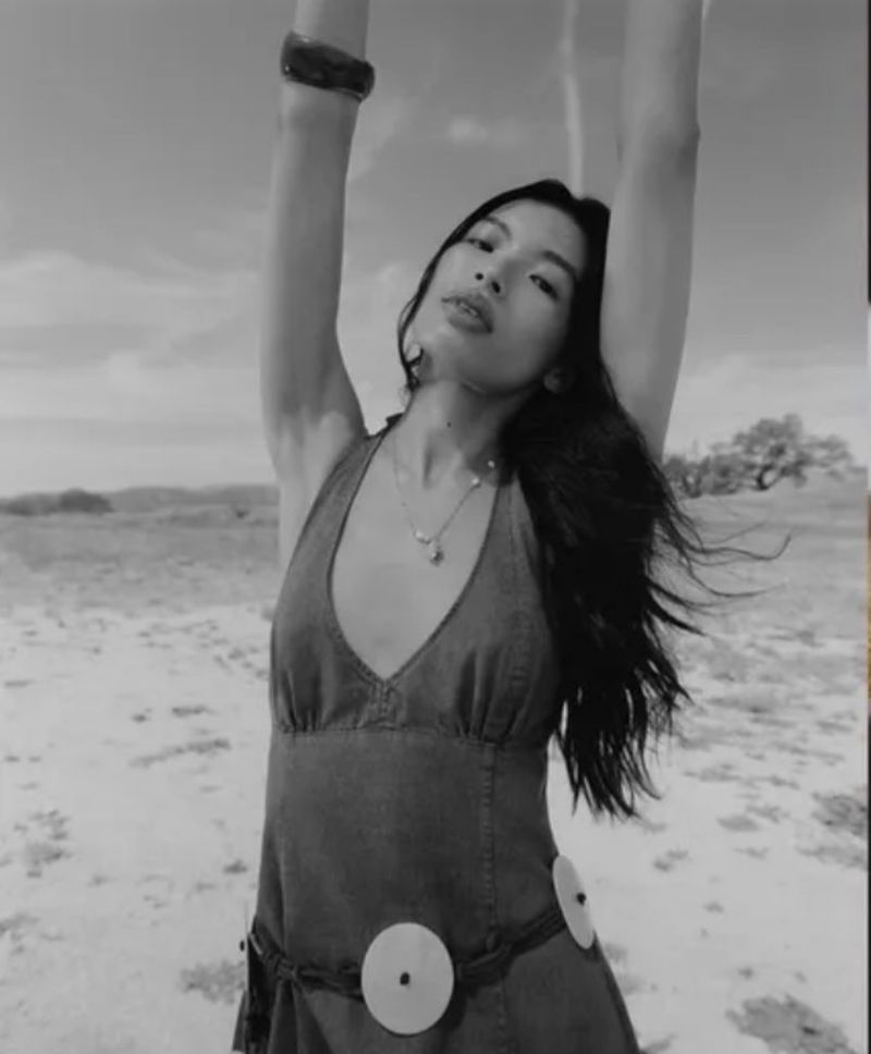 Model with arms raised wearing a halter dress against an outdoor landscape background