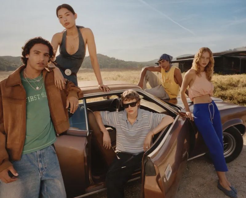 Group of diverse models posing around a brown vintage car in a grassy landscape for Zara Festival Collection.