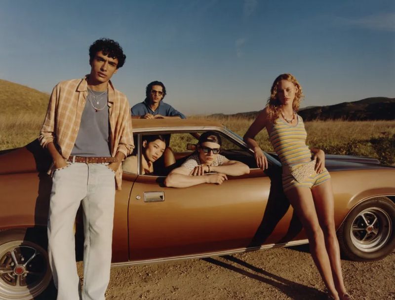 Group of models posing outdoors around a vintage brown car under warm sunlight for Zara.