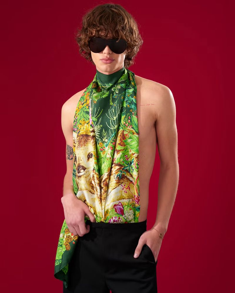Model wearing a green patterned silk scarf and black trousers against a deep red background