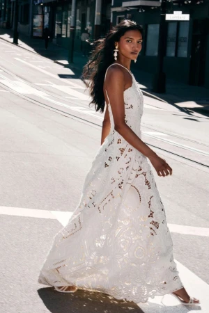 Model wearing a white lace bridal dress walking down a sunlit city street