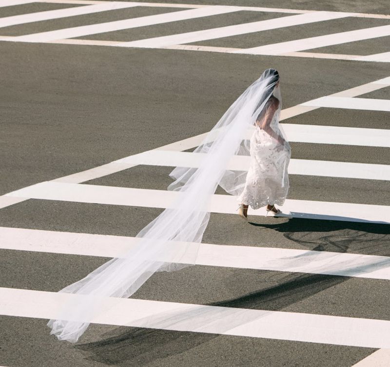 Model in white bridal dress with long veil walking across pedestrian crosswalk from above