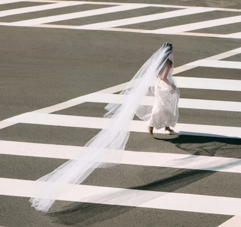 Model in white bridal dress with long veil walking across pedestrian crosswalk from above