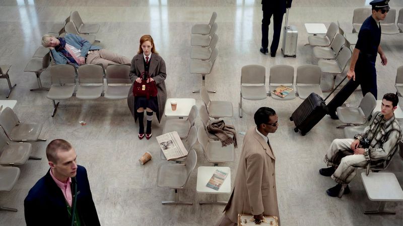 High angle shot of people waiting in an airport terminal seating area with chairs, luggage, and a magazine on the floor.