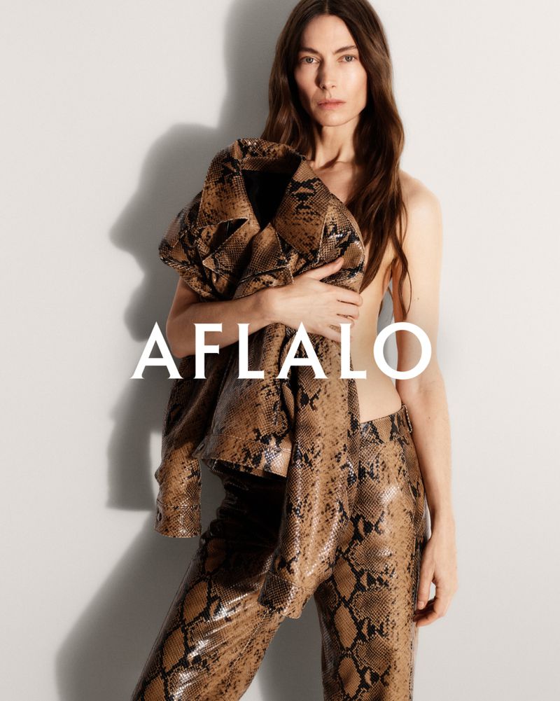 Woman in snakeskin print jacket and pants poses in a studio. Fashionable pose and neutral facial expression in a full shot.