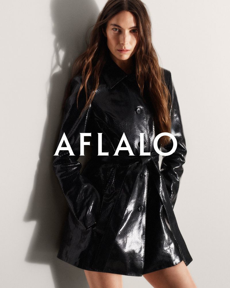 Model wearing a glossy black trench coat standing against a pale wall with dramatic shadow for Aflalo