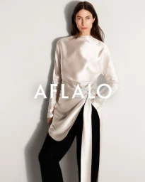 Model Jessica Miller wearing a long white silk top and black trousers against a neutral white seamless studio background.