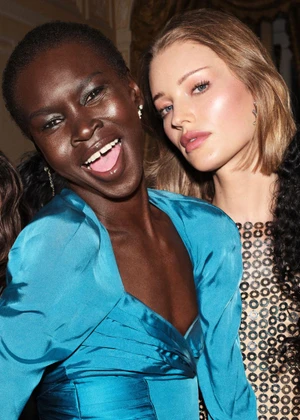 Close-up portrait of two female models smiling, one in a vibrant blue satin top and the other in a sequined dress.