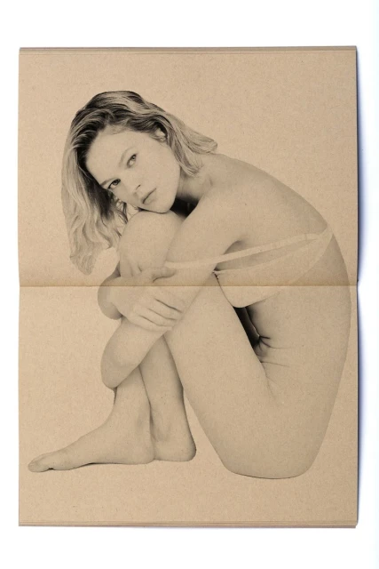 Monochrome portrait of a fair-skinned woman in a seated pose hugging her knees on a folded beige newspaper background.