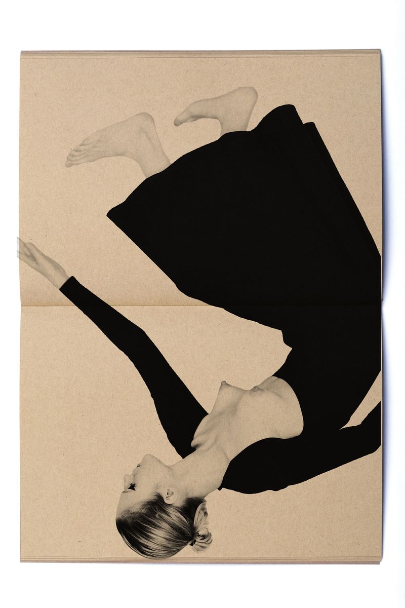 Monochrome art photo of a woman in a black dress with bare feet, upside down on a beige background, evoking a fine art editorial.