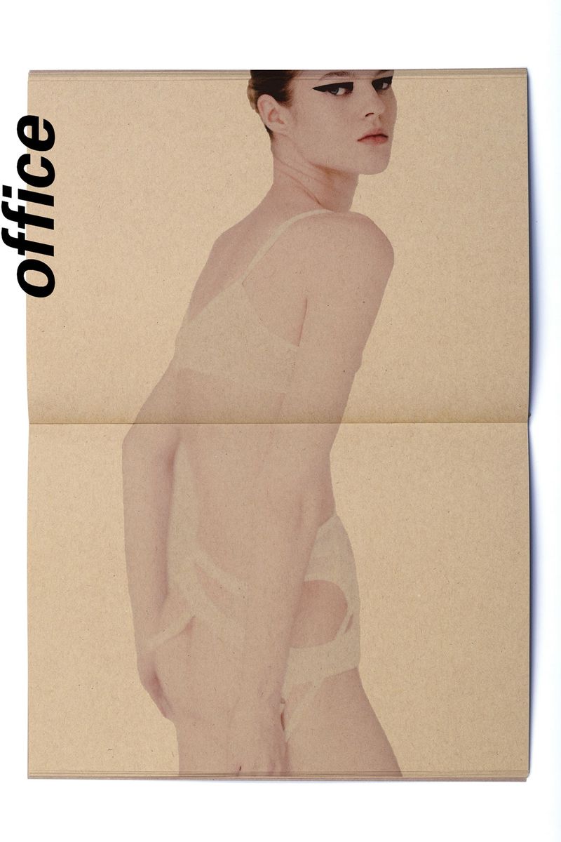 A woman poses wearing a lace bra and underwear, over a folded newspaper with a blurred effect, in a beauty and fashion editorial shot.