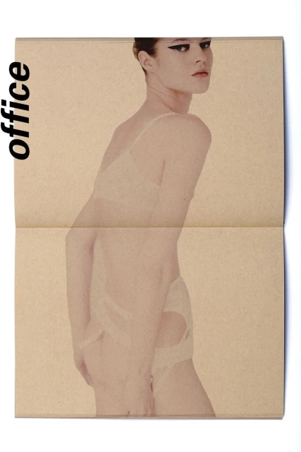 A woman poses wearing a lace bra and underwear, over a folded newspaper with a blurred effect, in a beauty and fashion editorial shot.