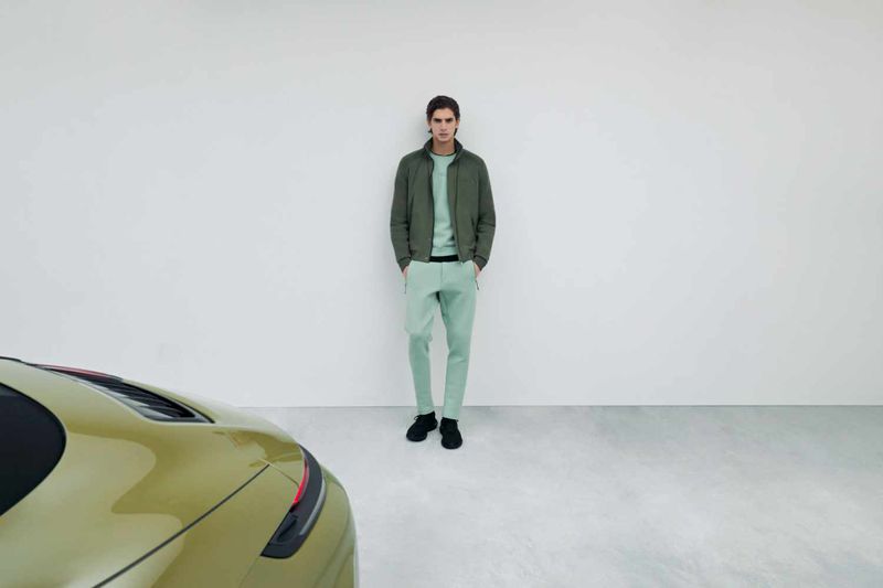Model wearing green apparel standing against a white wall next to a green car for the BOSS and Porsche campaign