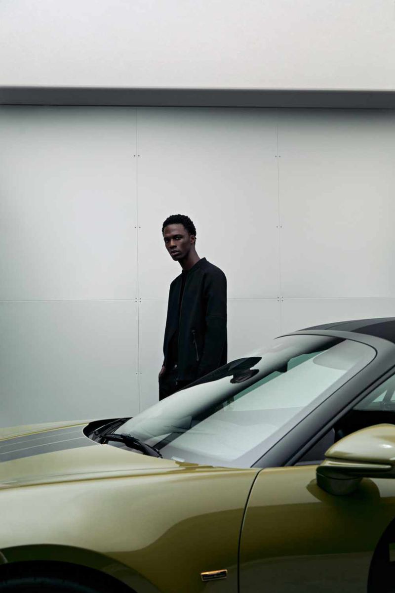 A man standing beside a green sports car against a plain white architectural backdrop for a BOSS and Porsche project.