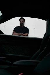 Model standing framed by car interior window, wearing a dark t-shirt against a white background.