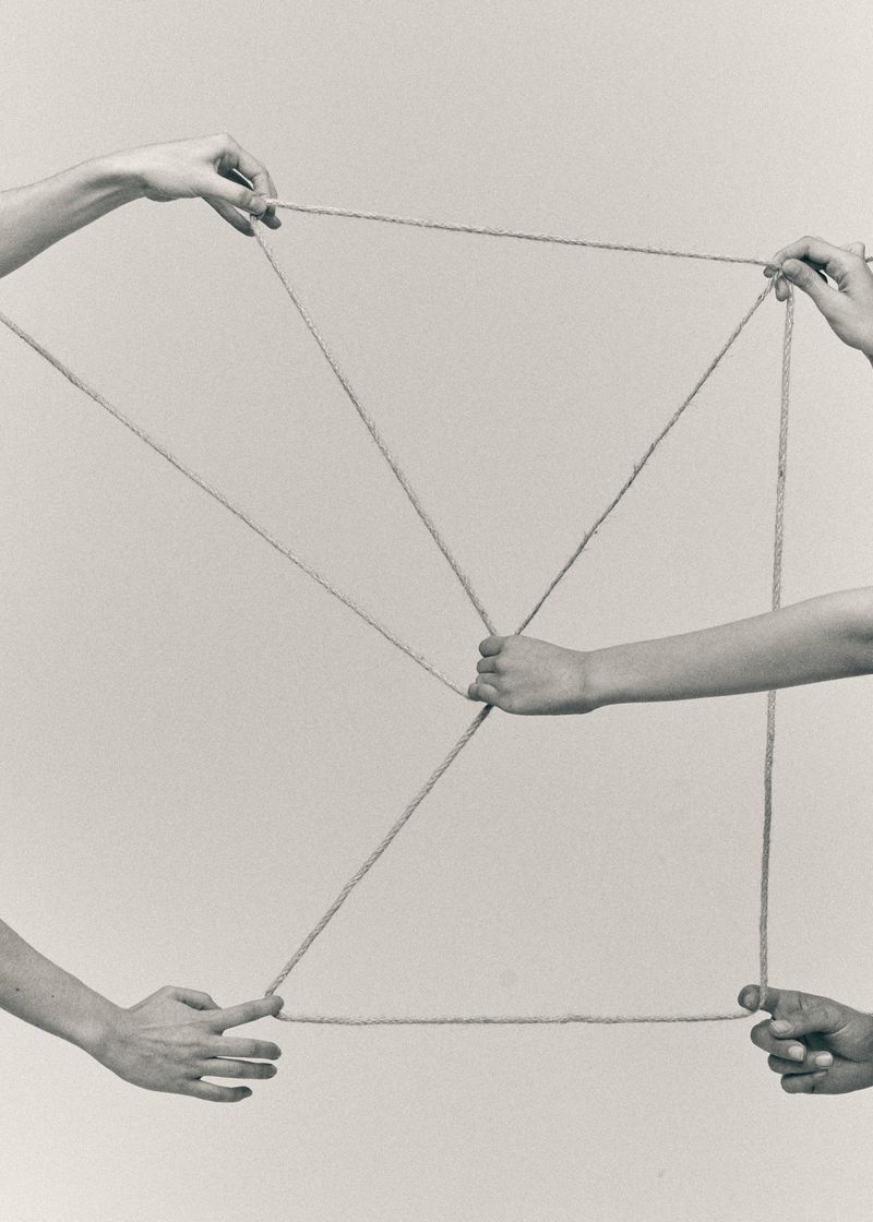 Multiple pairs of hands holding and stretching thin cords against a neutral background for Castaner
