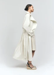 Model standing in profile wearing an ivory trench coat and espadrille wedge sandals against a white background