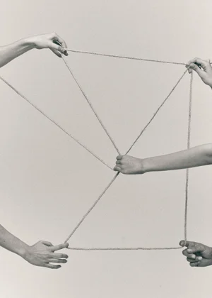 Multiple pairs of hands holding and stretching thin cords against a neutral background for Castaner
