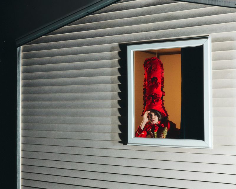 Model Lindsey Wixson wearing a towering red hat looking out a window for ICON Magazin Germany New in Town project