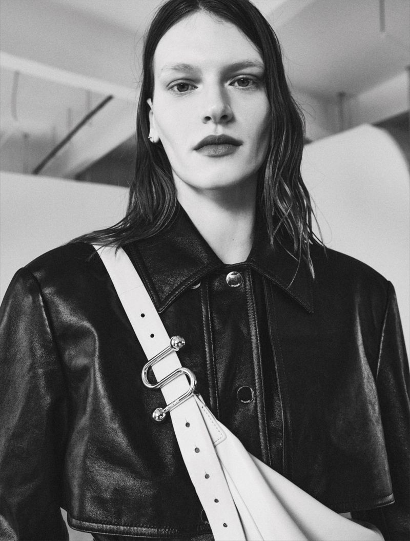 Model wearing a black leather jacket with a white strap crossbody bag in a monochrome fashion editorial portrait.