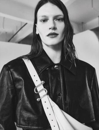 Model wearing a black leather jacket with a white strap crossbody bag in a monochrome fashion editorial portrait.