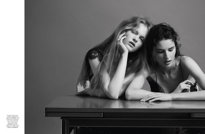 Two female models posing seated at a table against a plain grey studio backdrop in a black and white portrait photograph.