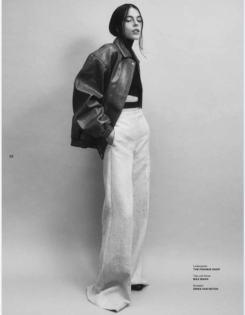 Model wearing an oversized leather jacket and light trousers against a neutral studio backdrop
