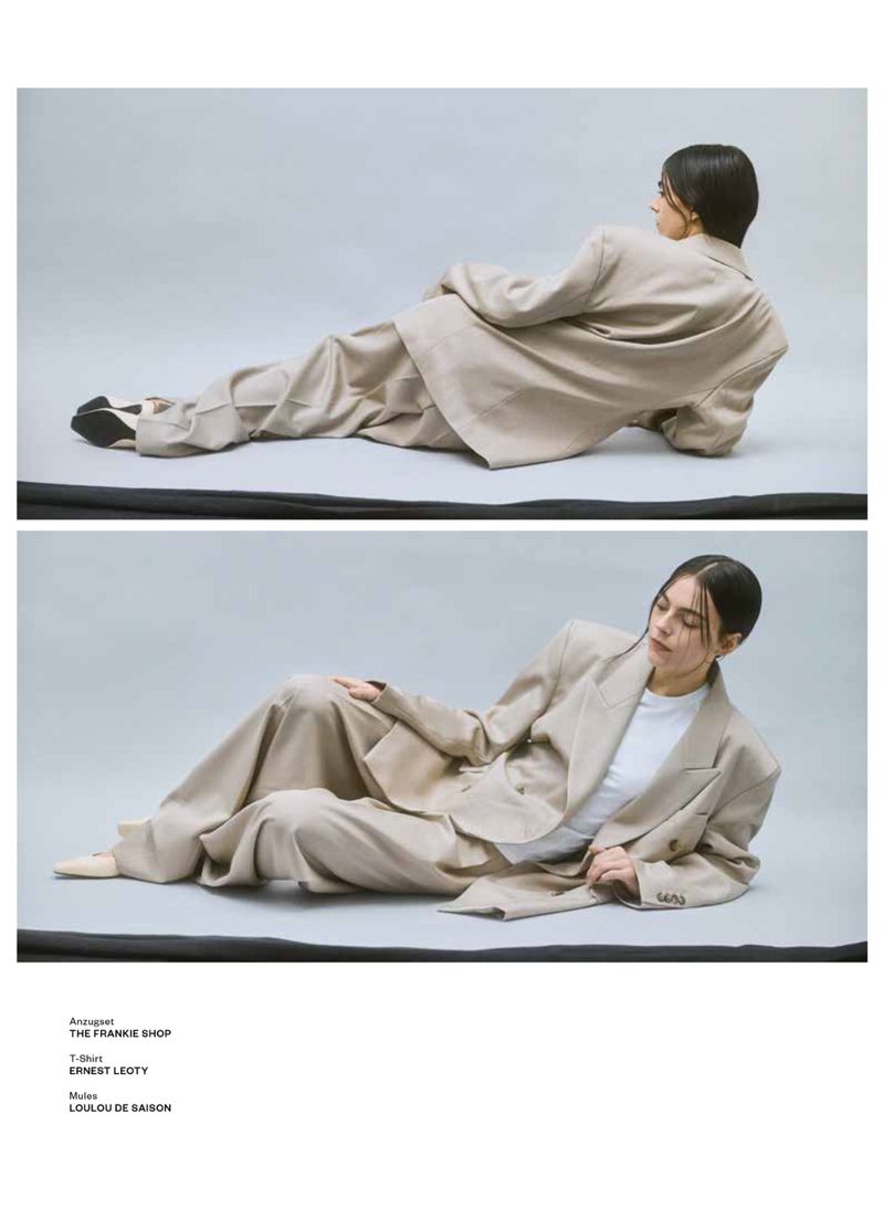 Two images show a model in a relaxed pose on a grey backdrop, wearing a light tan, oversized suit with a white t-shirt and loafers.