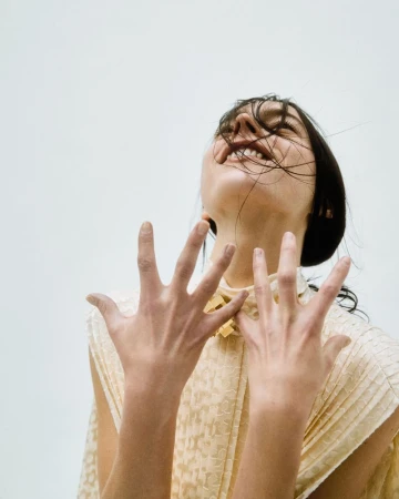 Model with dark hair laughing with hands raised up toward camera against a plain white background for Flair Germany Wondelbar