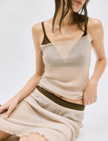 Model wearing a sheer cream top and matching skirt over dark undergarments against a plain white studio background.