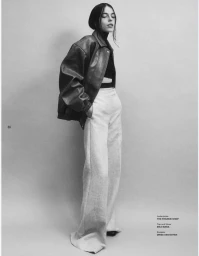 Model wearing an oversized leather jacket and light trousers against a neutral studio backdrop