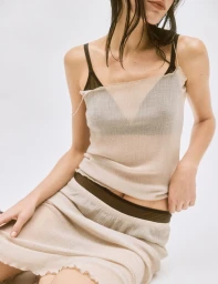 Model wearing a sheer cream top and matching skirt over dark undergarments against a plain white studio background.