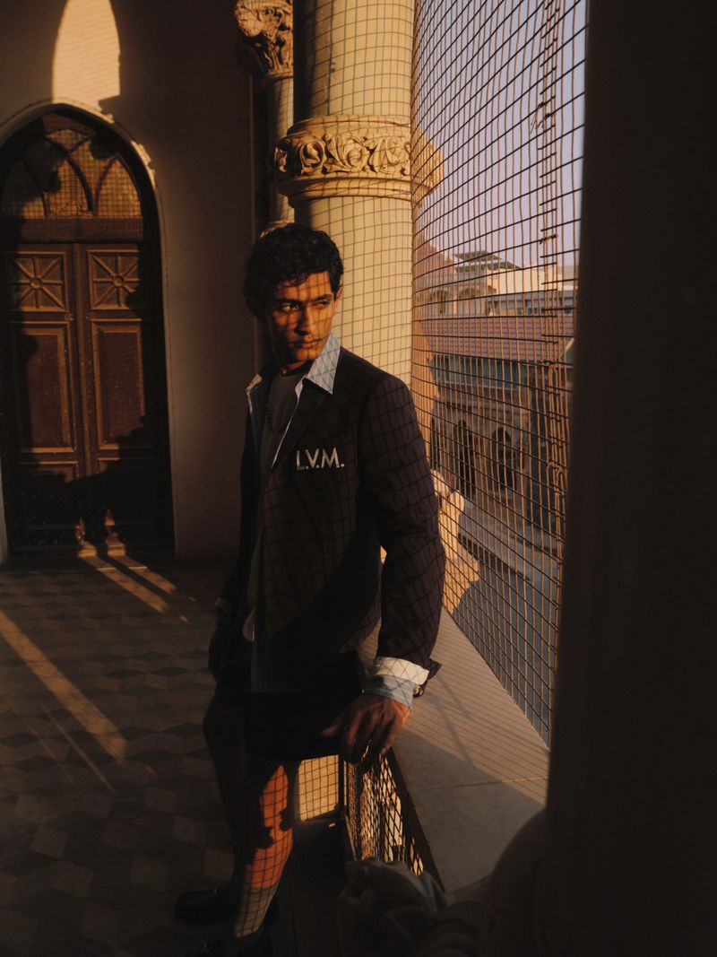 Man standing on a colonnade balcony next to a wire mesh screen during sunset for Justsmile editorial