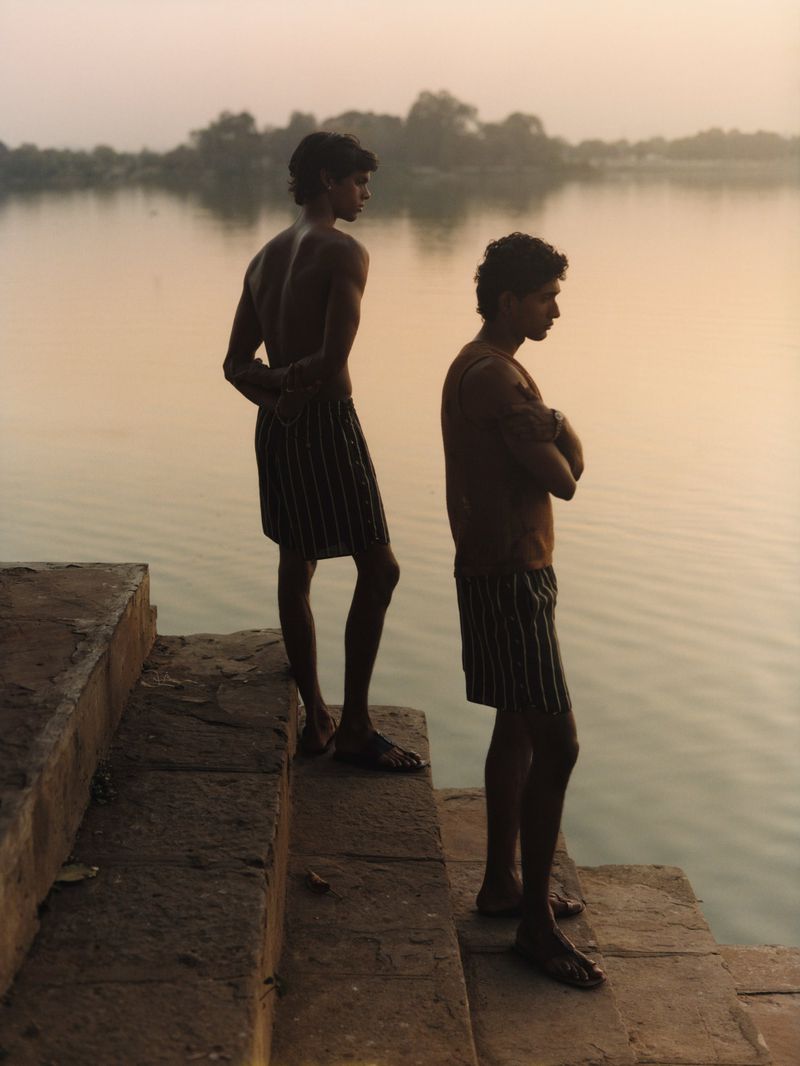 Two men standing on stone steps by a lake at sunset for Justsmile SS26 Editorial by Justsmile Magazine.