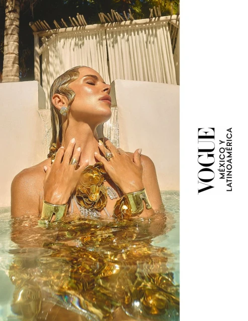 Woman in gold jewelry and water, Vogue Mexico, sunlight dappling water, palm tree, white curtains, outdoor setting, wet wavy hair.