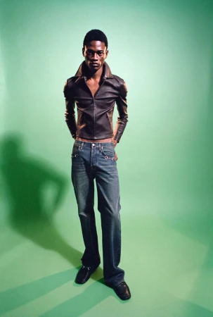 Model wearing dark leather jacket and denim jeans standing against a green backdrop for SSAW Magazine