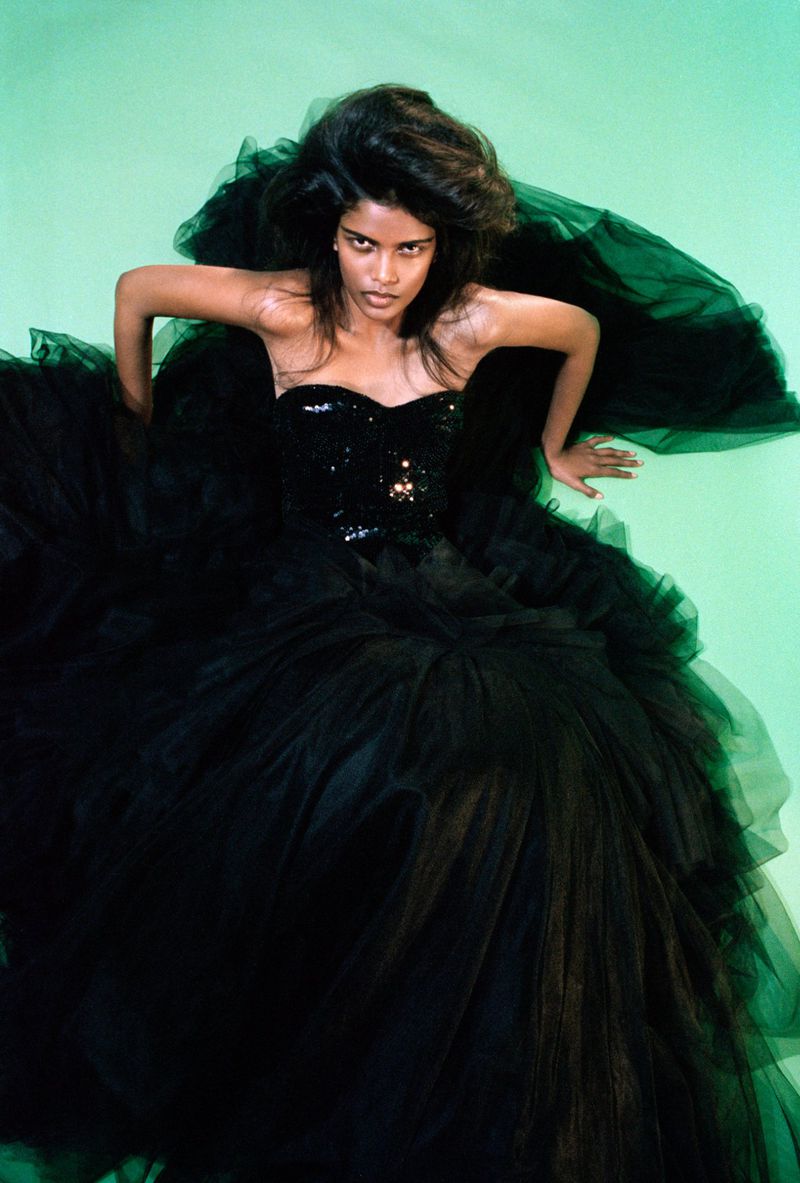 Woman with dark hair and dark strapless dress poses against a bright green background in a studio setting. High angle shot.