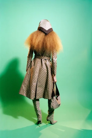 Model from behind wearing patterned coat, headscarf, and boots against a green background