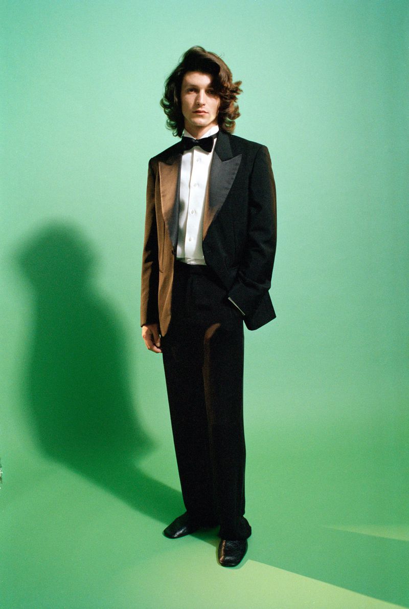 Man wearing a black tuxedo with brown jacket panels and a bow tie against a green seamless background for Gucci AW26.