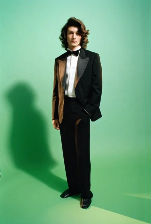 Man wearing a black tuxedo with brown jacket panels and a bow tie against a green seamless background for Gucci AW26.