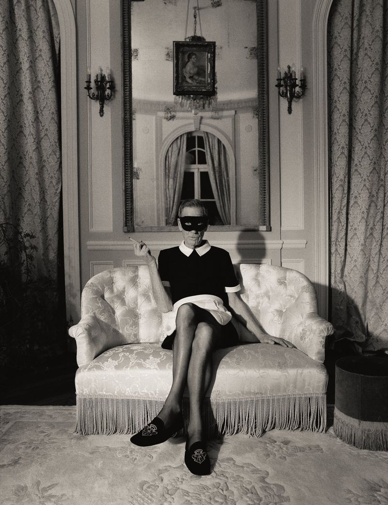 Model wearing a black eye mask and maid costume seated on an ornate sofa in a formal interior for Re-Edition Magazine print