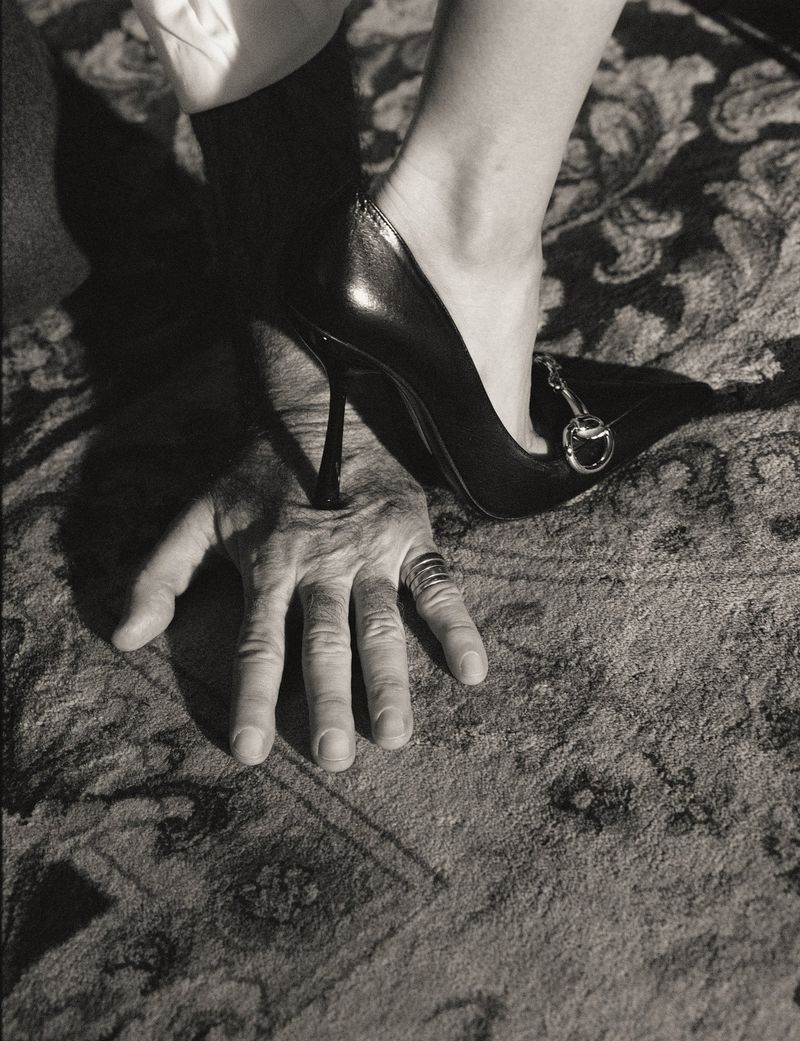 Close-up of a high-heeled shoe stepping on a man hand resting on patterned carpet