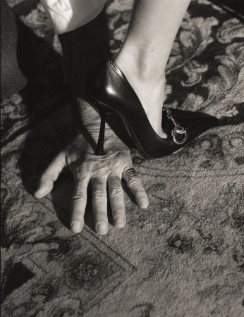 Close-up of a high-heeled shoe stepping on a man hand resting on patterned carpet