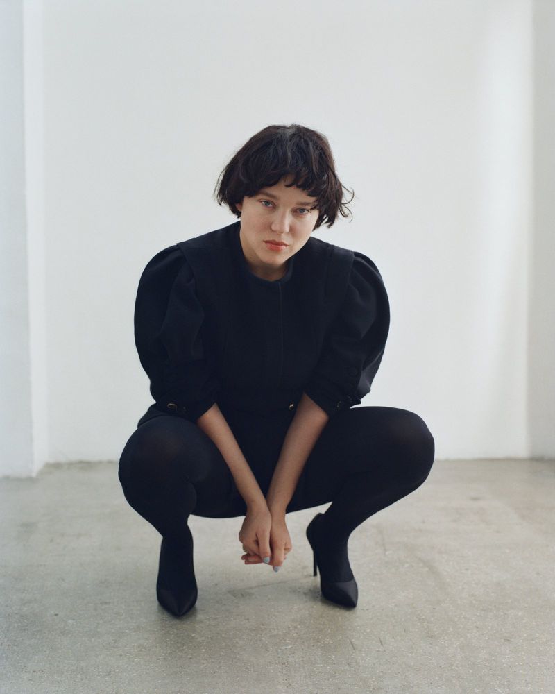 French actress Léa Seydoux crouching in a black outfit against a plain white studio wall